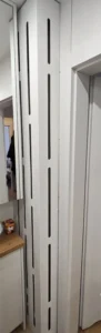 Wysoki biały panel z pionowymi otworami przy drzwiach