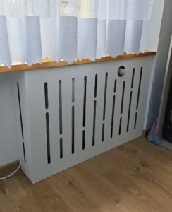 Krótka biała maskownica grzejnika pod firanką i parapetem